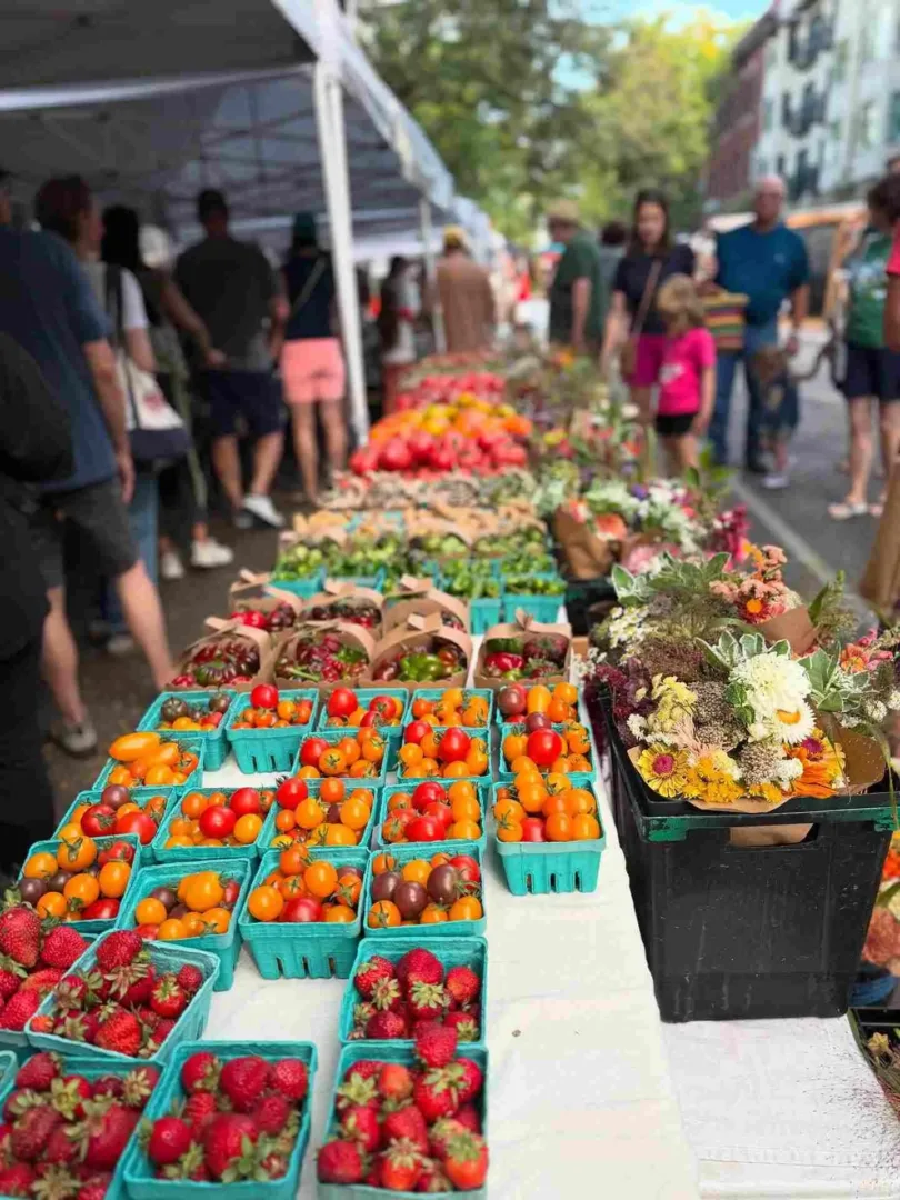 A vibrant farmer's market in Seattle in April with baskets of fresh strawberries, colorful tomatoes, and bouquets of flowers on display.