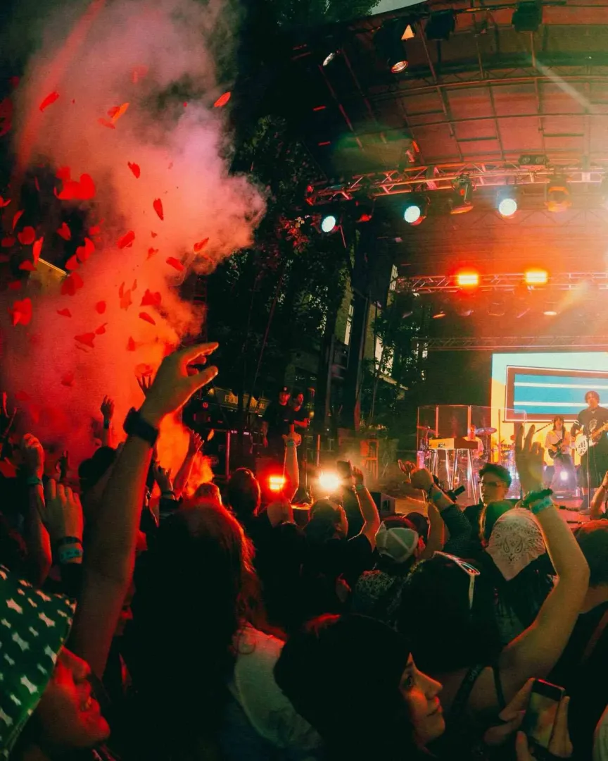 A concert crowd with hands raised and red confetti falling at an outdoor festival in Seattle in July.