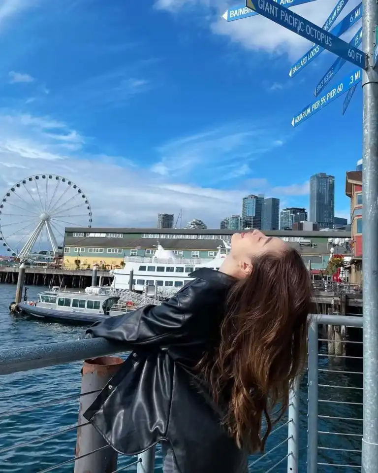 A woman leans back by the waterfront near the vibrant International District Seattle with a ferris wheel.