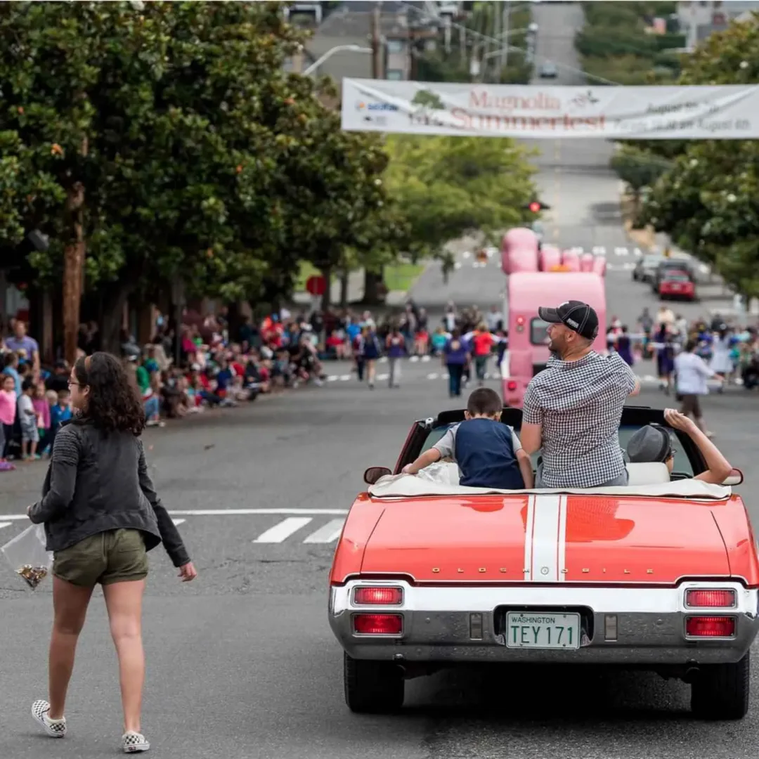 The Magnolia Summerfest parade includes a vintage red convertible and crowds in Seattle in August.
