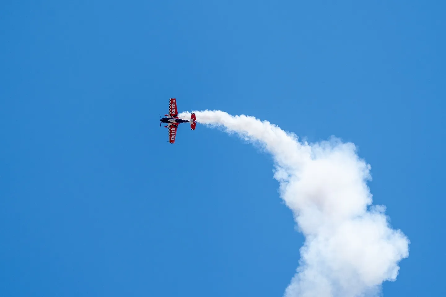 A red and white stunt plane loops and trails white smoke in a bright blue sky over Seattle in June.
