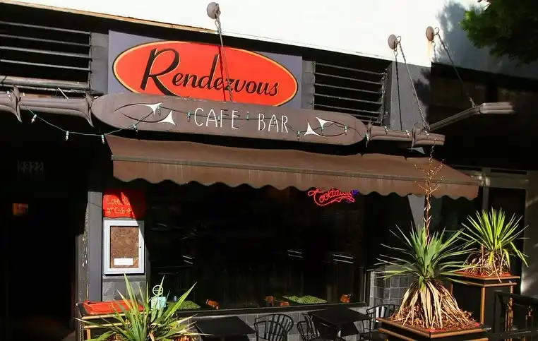 Rendezvous Cafe Bar entrance in Belltown Seattle with a brown awning, oval sign, and potted plants.