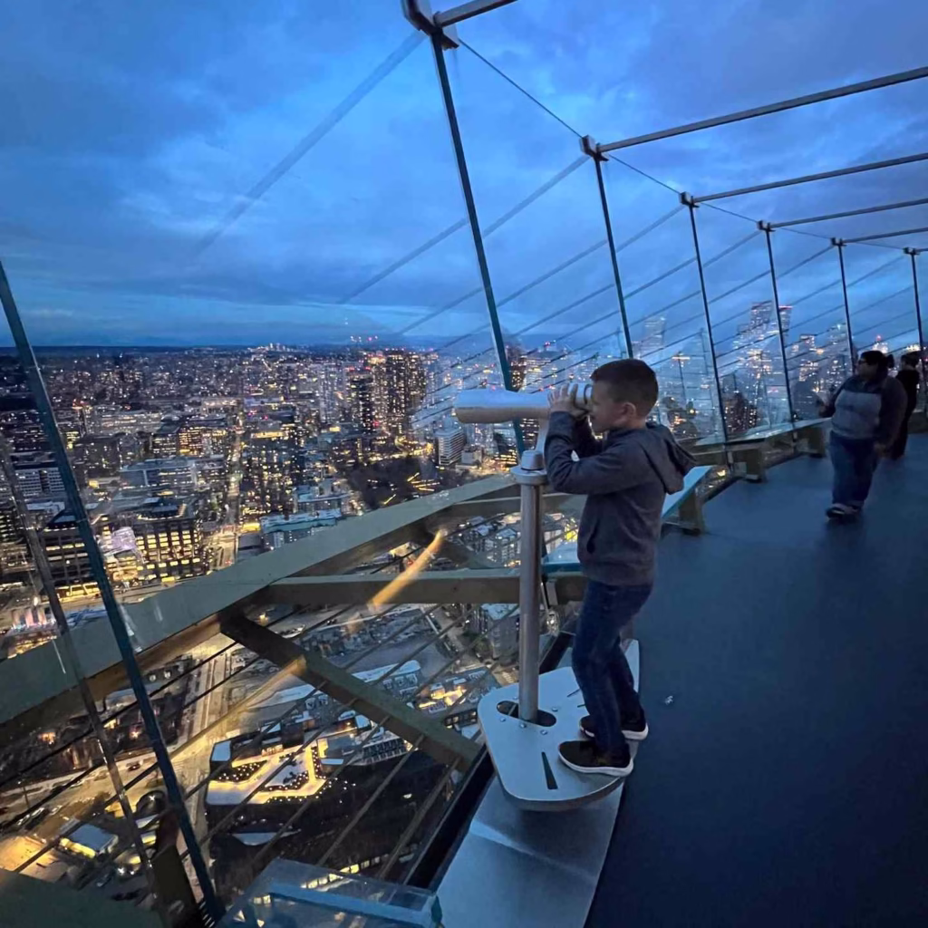 A young boy looks through a telescope at the city lights while getting around Seattle attractions.