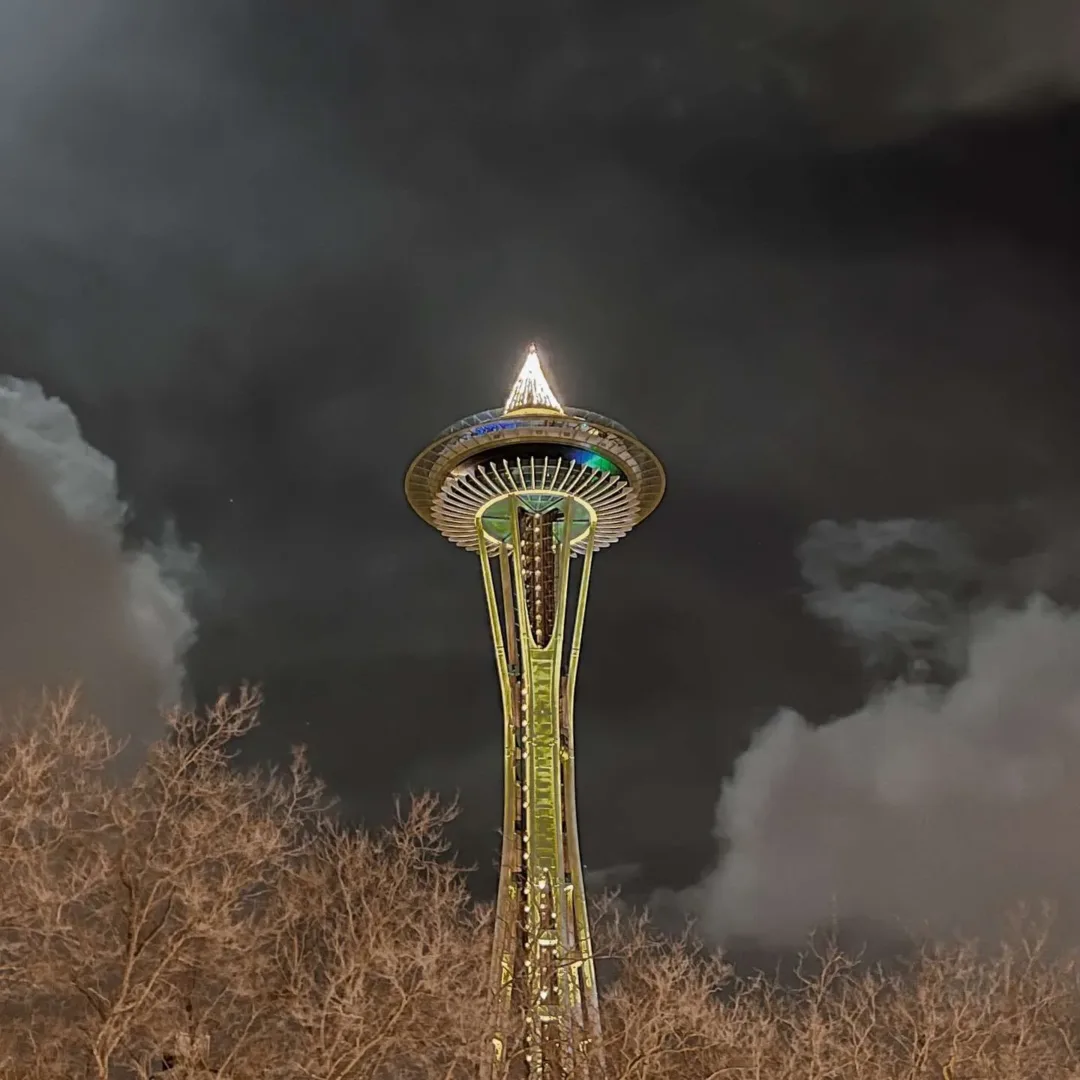 The Space Needle glows with lights against a cloudy night sky in Seattle in July.