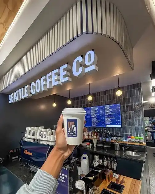 A person holds a branded cup inside a modern cafe, highlighting the downtown Seattle coffee culture.