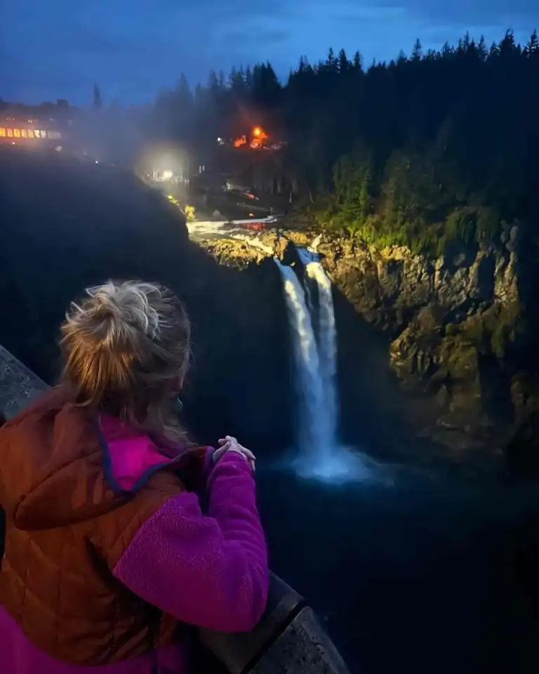 A woman in a pink jacket views the illuminated water during a Snoqualmie Falls Tour.