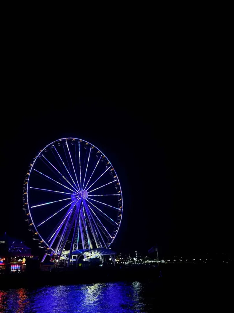 The Seattle Great Wheel glows purple over Elliott Bay near the Chihuly Garden and Glass guide.