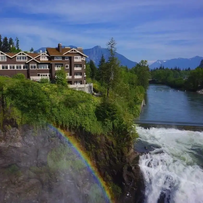 A vibrant rainbow arches over the rushing waterfall and lodge during a scenic Snoqualmie Falls Tour.