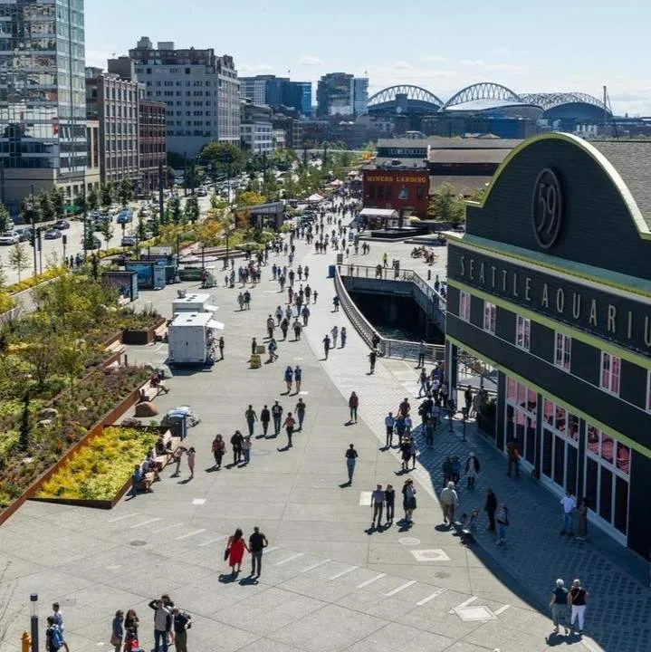 Crowds gather outside the Seattle Aquarium on a sunny day, using a Chihuly Garden and Glass guide.